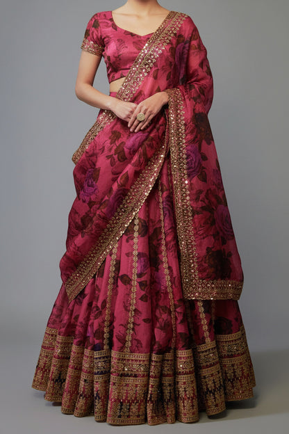 Pink saree with floral patterns and gold embroidery on a gray background