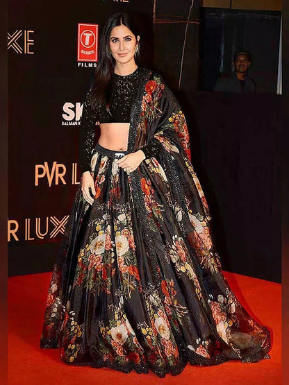 Person wearing a floral and black outfit on a red carpet with logos in the background